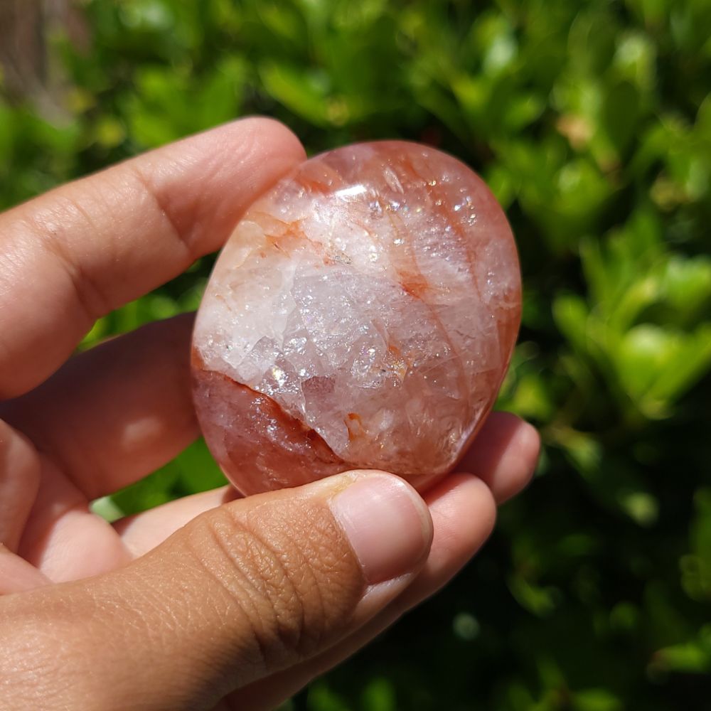 Hand holding a hematoid quartz palm stone with a green blurred background