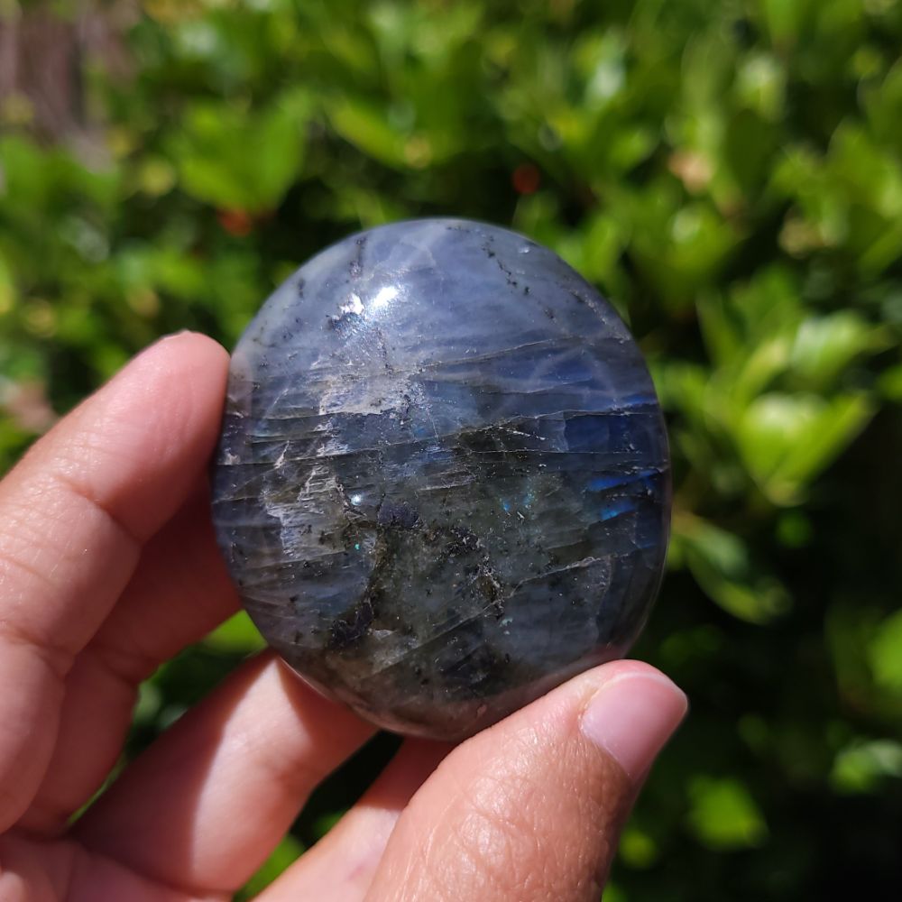 Hand holding a labradorite palm stone against a green outdoor background