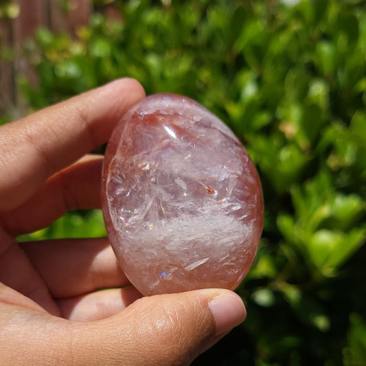 Hand holding a Fire Quartz palm stone with a blurred green background