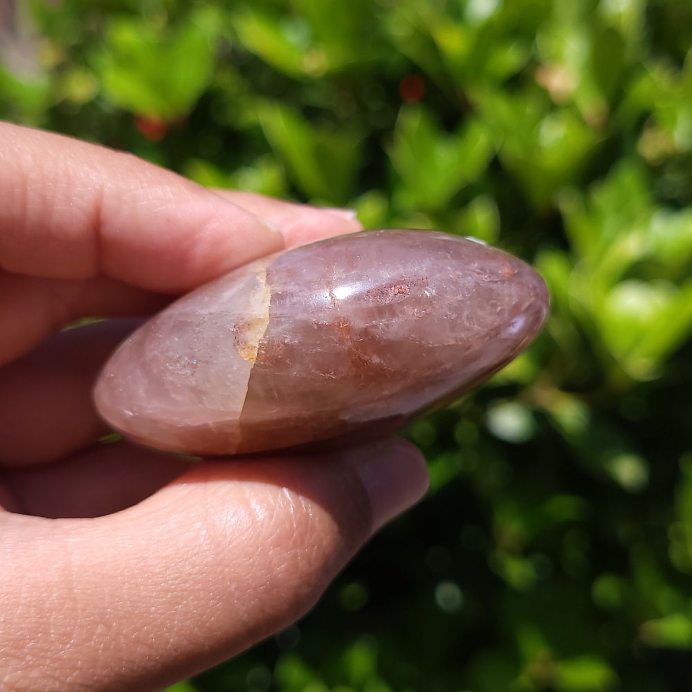 Hand holding a Fire Quartz palm stone with a blurred green background