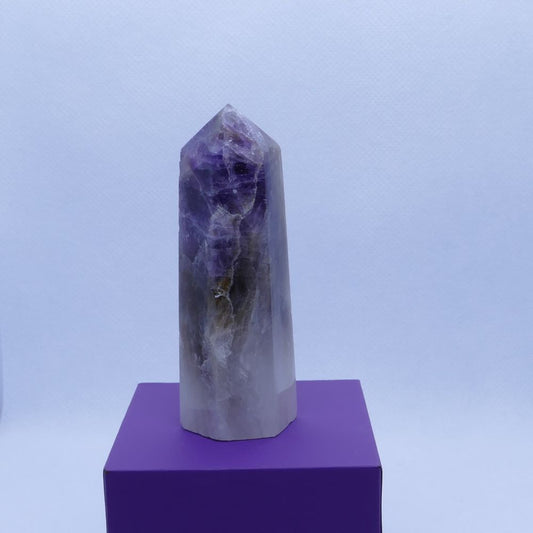 purple amethyst, brown smoky quartz and white quartz healing crystals tower on a purple box and white background, seller dumi's crystals