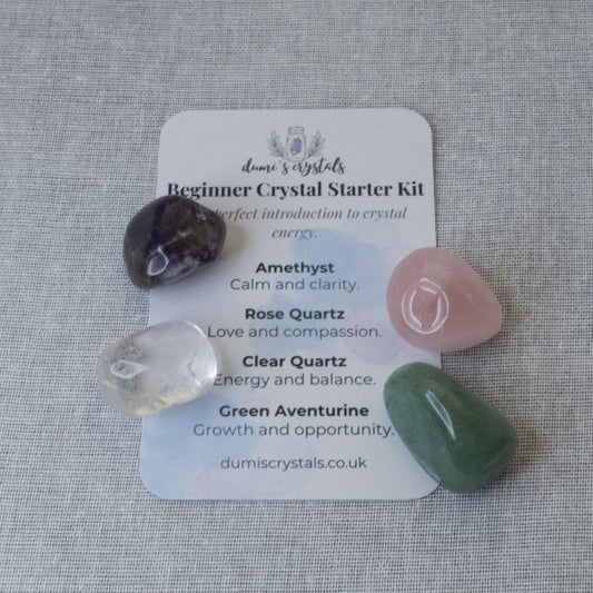Crystal starter kit with amethyst, clear quartz, rose quartz and green aventurine on a card on a textured surface.