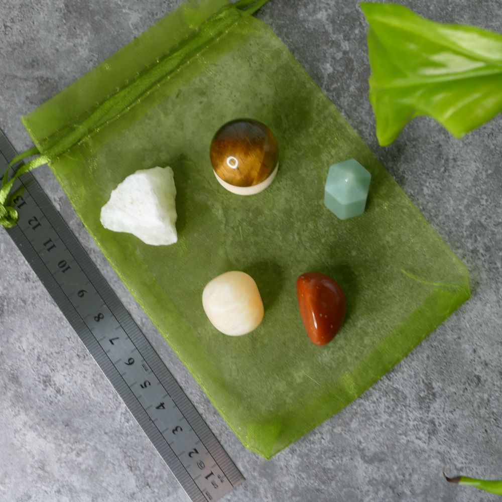 Green drawstring bag with various stones on a gray surface, ruler for scale.
