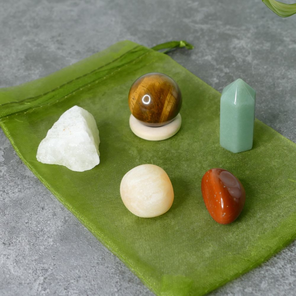 Collection of raw lemon quartz, tiger's eye sphere, green aventurine mini tower, orange calcite and red jasper tumbled stones on a green fabric against a gray background
