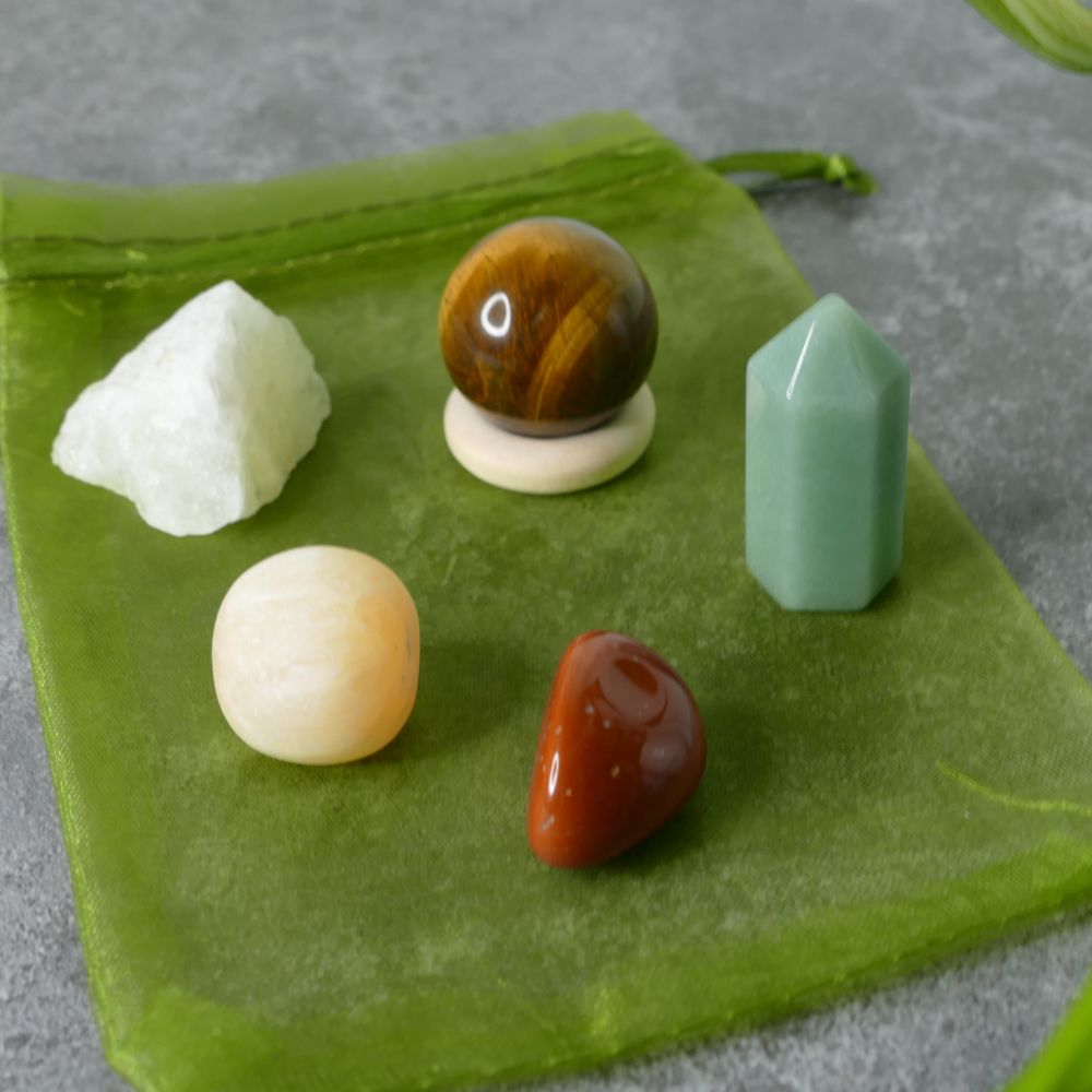 Set of raw lemon quartz, tiger's eye sphere, green aventurine mini tower, orange calcite and red jasper tumbled stones on a green fabric background