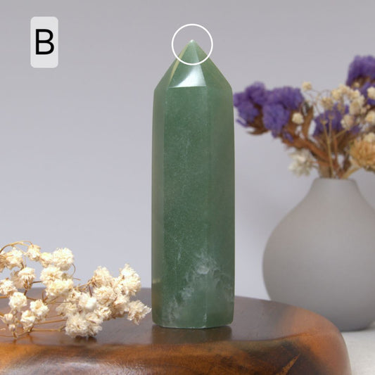 Green aventurine crystal on a wooden surface with flowers in the background