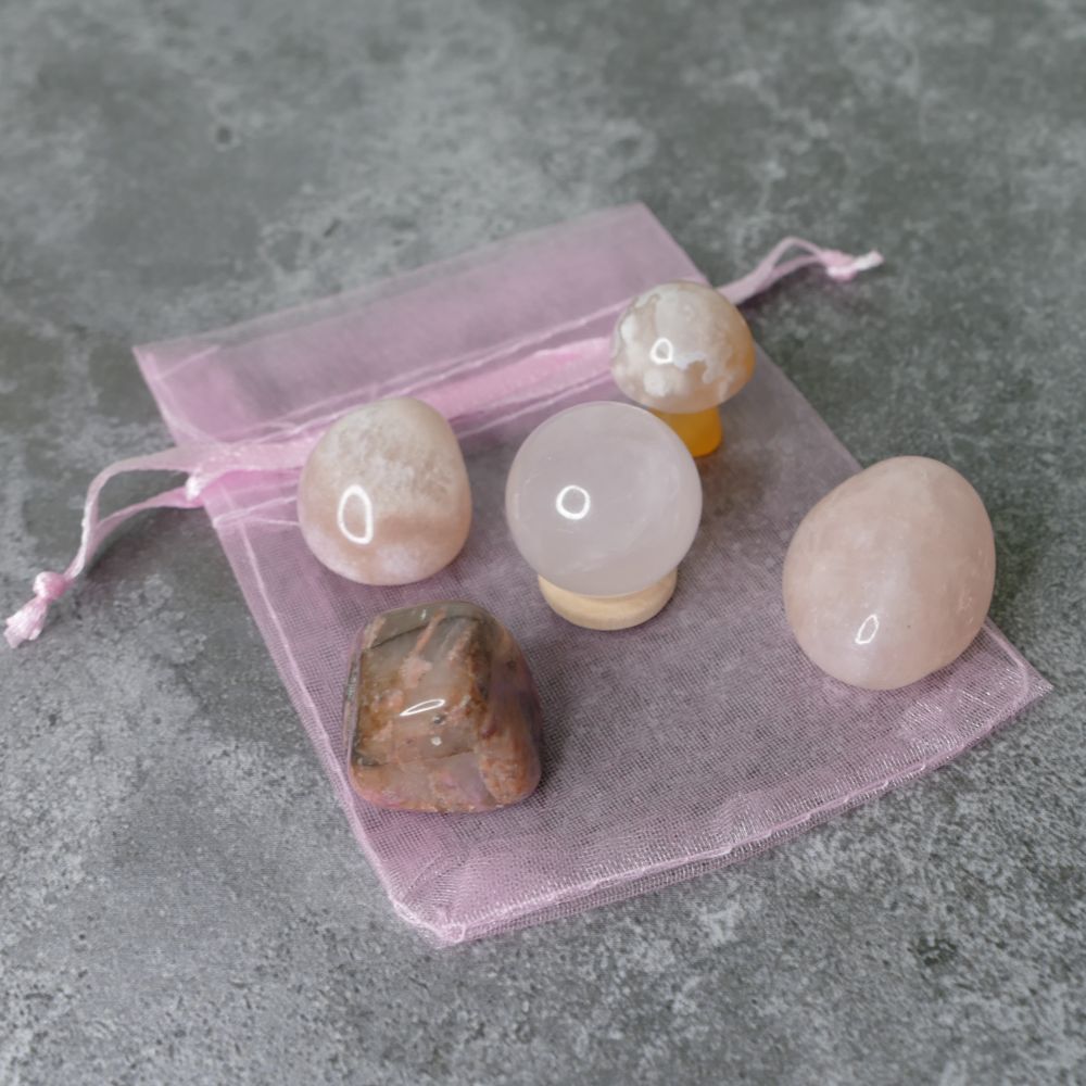 Set of polished stones on a pink drawstring bag against a gray concrete background