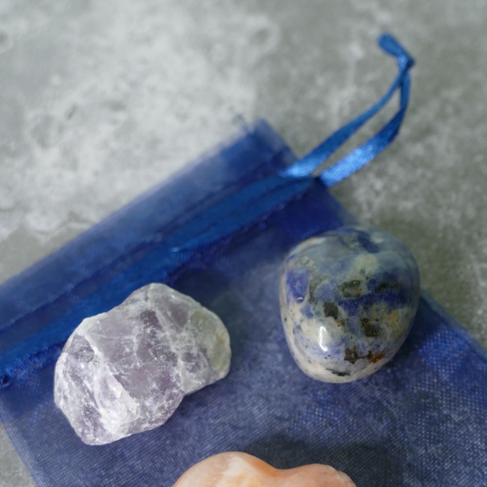 A fluorite rough stone and a sodalite tumbled stone on a blue fabric background