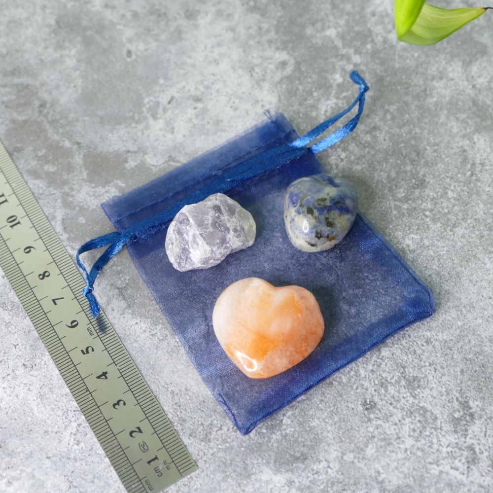Three crystals fluorite, sodalite and carnelian on a blue drawstring bag with a ruler for scale on a gray surface
