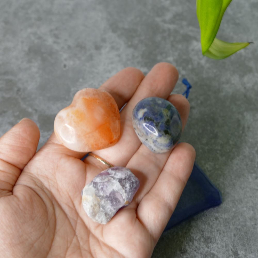 Hand holding three colourful stones fluorite, sodalite and carnelian against a gray background
