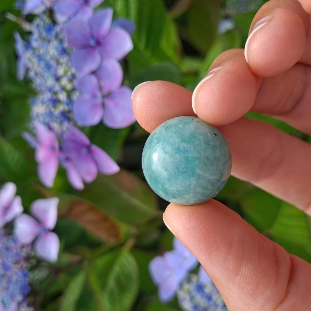  Dumi's Crystals | Amazonite Mini Sphere (20mm) | A close-up view of a captivating Amazonite Mini Sphere, showcasing its smooth, polished surface and mesmerizing blend of green and blue hues. This 20mm sphere radiates calming energy, promoting peace, communication, and emotional balance.