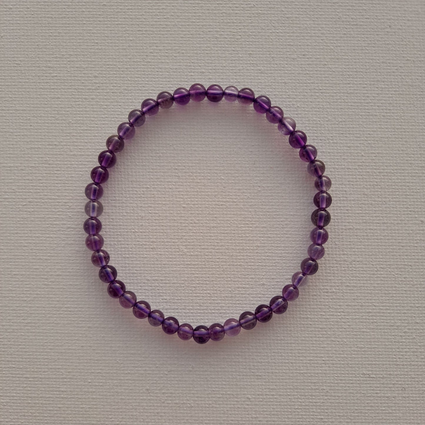 A stretch amethyst handmade bracelet with 4mm round beads displayed on a white background, from Dumi's Crystals. The perfectly spherical amethyst beads are evenly strung together, revealing their rich purple colour and smooth texture.