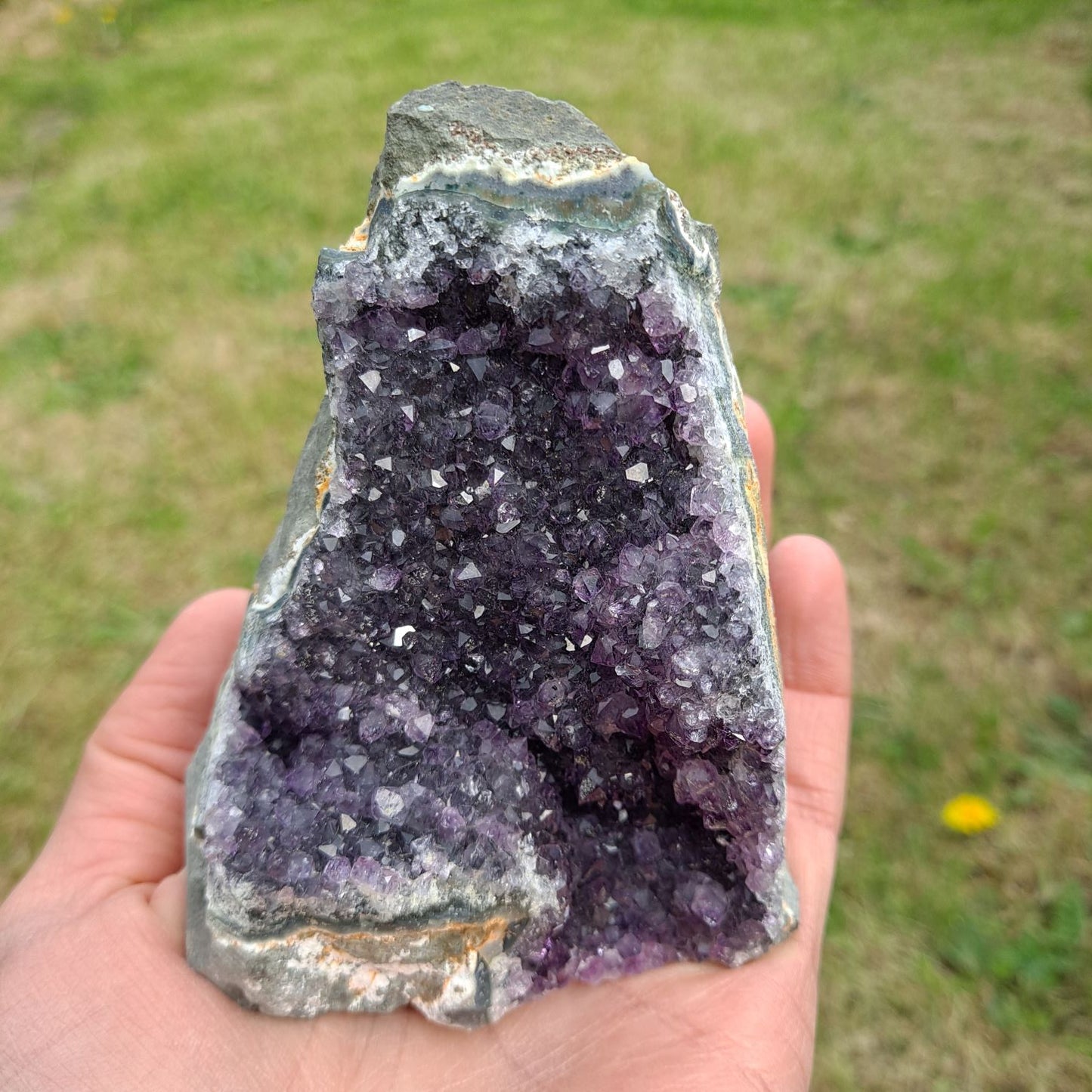 Dumi's Crystals | Amethyst Cluster (Portable, 9cm) in hand (side view) | Feel the intricate crystals of this Amethyst Cluster (9 x 7.6 x 7.6cm) as you hold it in your hand. Let its gentle energy wash over you, promoting relaxation and emotional balance.