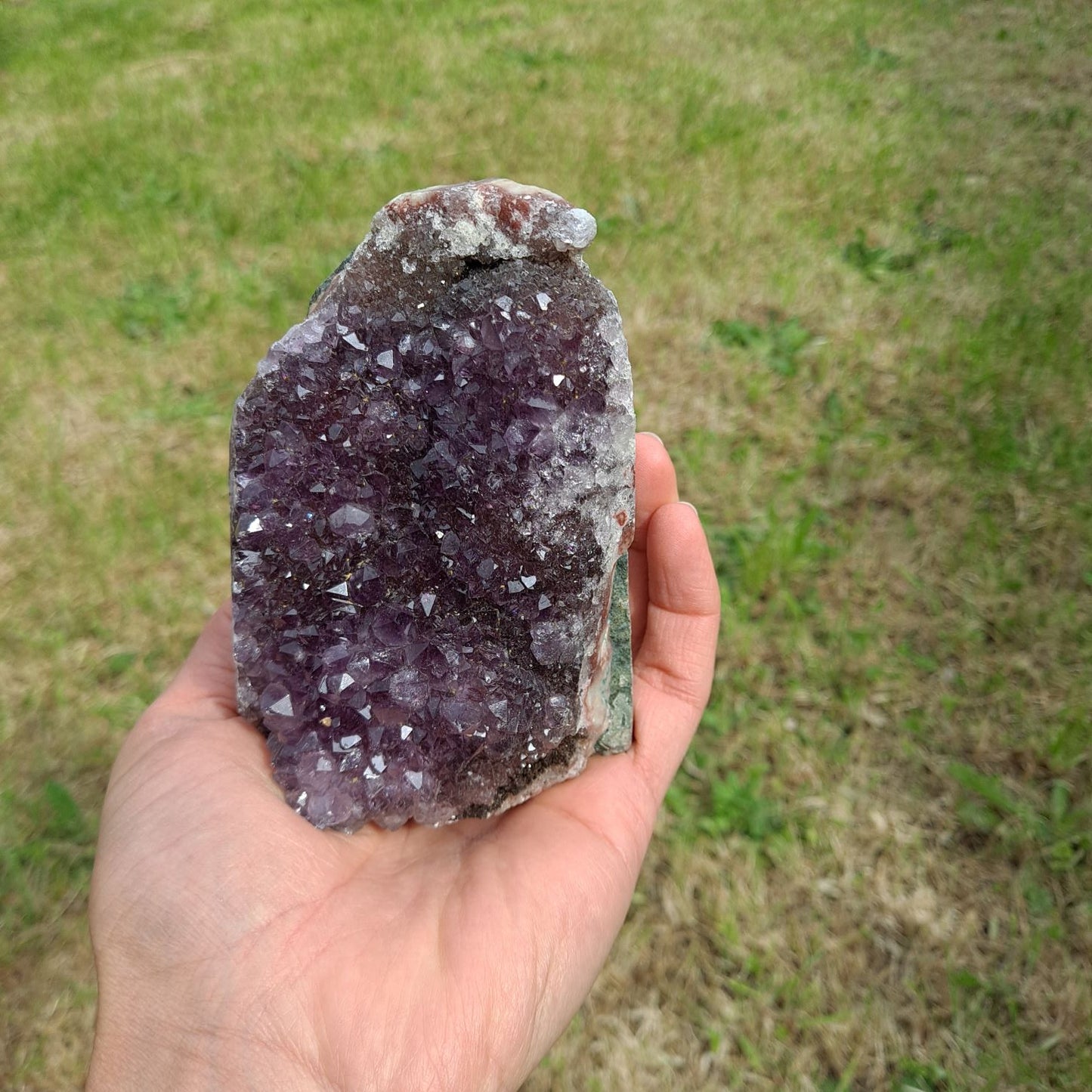 Dumi's Crystals | Amethyst Cluster (10.6cm, Striking) in hand (side view) | Feel the intricate crystals of this Amethyst Cluster (10.6 x 6.3 x 6.9cm) as you hold it in your hand. Its comfortable size allows you to connect with its calming energy, promoting relaxation and emotional balance.