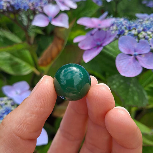 Dumi's Crystals | Green Agate Mini Sphere (20mm) | A close-up view of a captivating Green Agate Mini Sphere, showcasing its vibrant green hues and unique patterns. This 20mm sphere is believed to promote peace, emotional balance, personal growth, and a connection with nature. It's also thought to soothe the heart and mind while fostering inner peace.