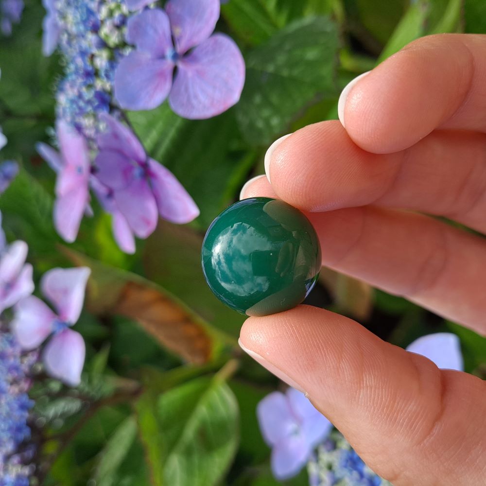 Dumi's Crystals | Green Agate Mini Sphere (20mm) | A close-up view of a captivating Green Agate Mini Sphere, showcasing its vibrant green hues and unique patterns. This 20mm sphere is believed to promote peace, emotional balance, personal growth, and a connection with nature. It's also thought to soothe the heart and mind while fostering inner peace.