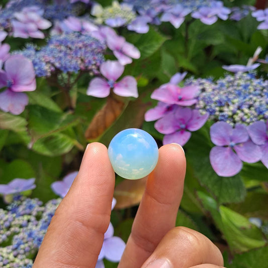 Dumi's Crystals | Opalite Mini Sphere (20mm) | A close-up view of a captivating Opalite Mini Sphere, showcasing its vibrant play of color and smooth surface. This 20mm, man-made stone is believed to promote peace, serenity, and personal growth. It's also thought to enhance intuition and spiritual connection.