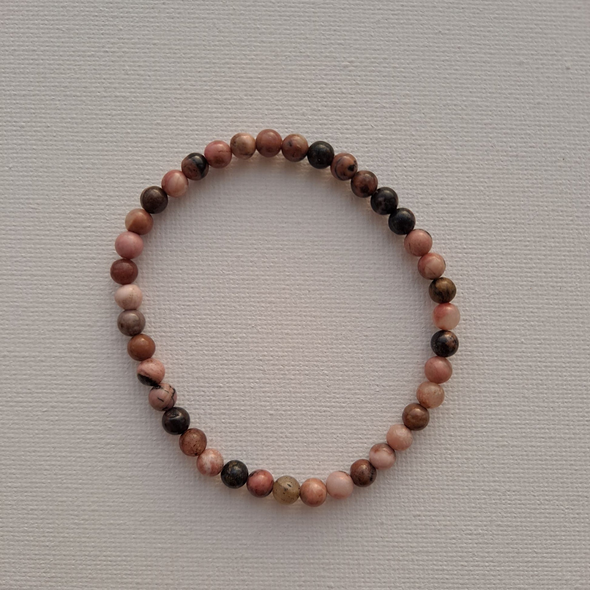 Dumi's Crystals | 4mm Rhodonite Stretch Bracelet (7 Inch) | Close-up of a handcrafted bracelet featuring genuine 4mm Rhodonite beads in soft pink hues with contrasting dark veins. Rhodonite is known as the stone of compassion and is believed to promote emotional healing and self-love.