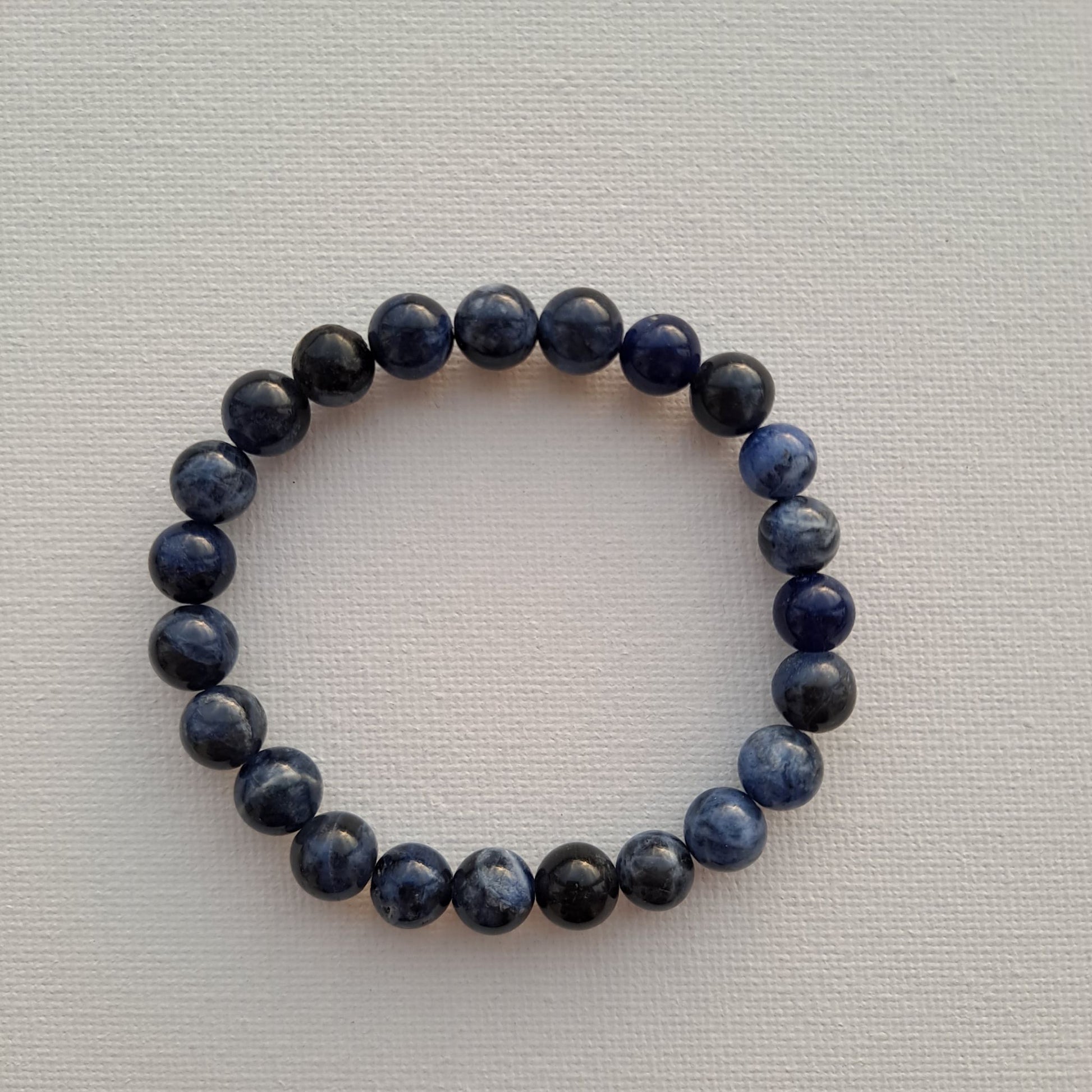 Dumi's Crystals | Sodalite Stretch Bracelet (7 Inch) | Close-up of a handcrafted bracelet featuring genuine 8mm beads in deep blue hues. Sodalite is known as the stone of truth and communication and is believed to promote clear communication, inner wisdom, mental clarity, and emotional balance.