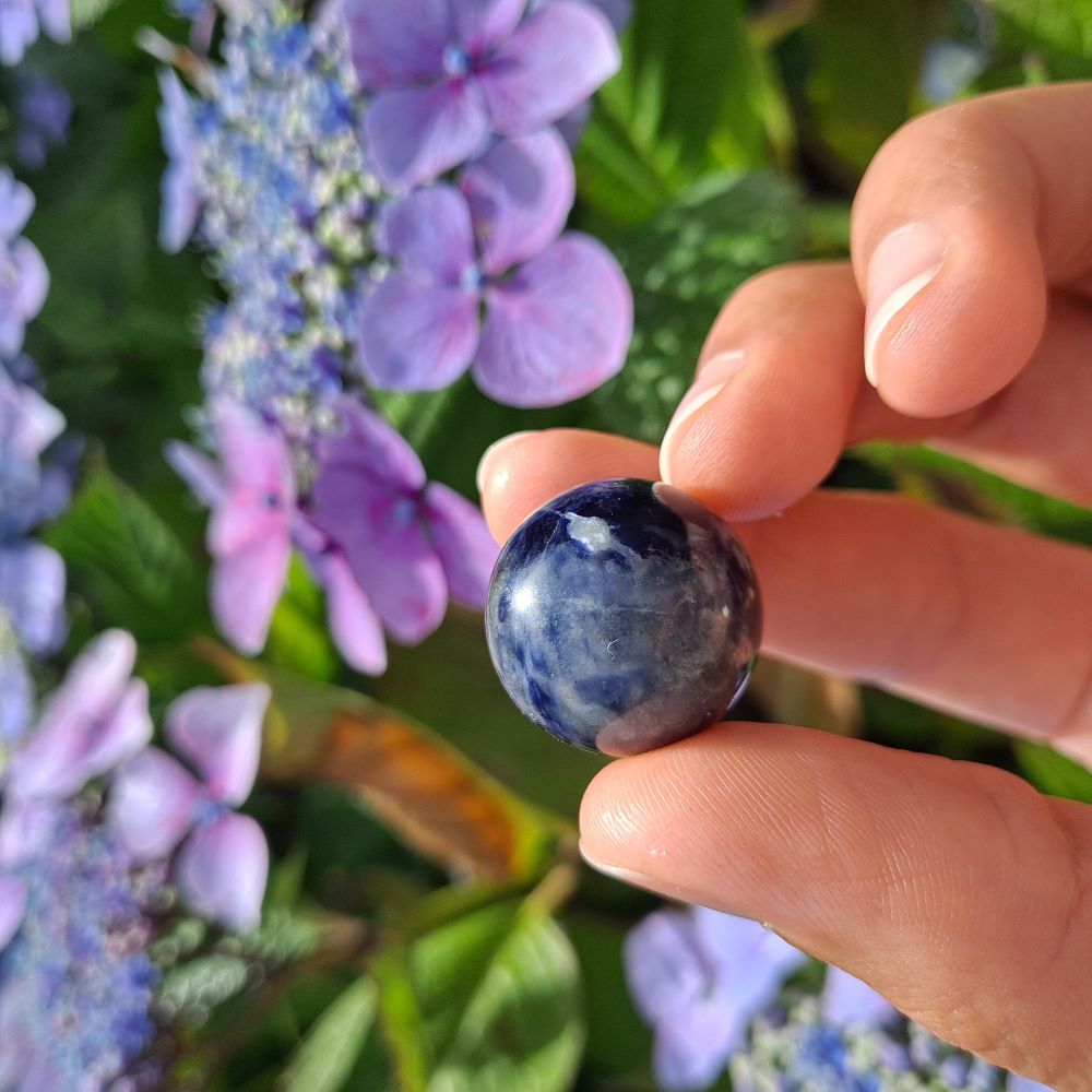 Dumi's Crystals | Sodalite Mini Sphere (20mm) | A close-up view of a captivating Sodalite Mini Sphere (20mm), showcasing its vibrant blue hues with flecks of white. This stone, known as the Stone of Logic, is believed to promote mental clarity, peace, and clear communication. It's also thought to reduce stress and boost confidence.