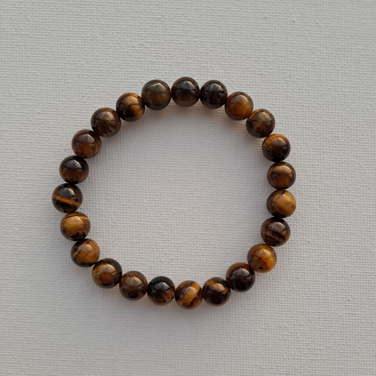 Dumi's Crystals | Tiger's Eye Stretch Bracelet (7 Inch with 8mm Beads) | Close-up of a handcrafted bracelet featuring genuine 8mm Tiger's Eye beads with captivating golden-brown hues and a touch of shimmer. Tiger's Eye is known as the stone of courage and protection and is believed to promote strength, confidence, mental clarity, and prosperity.