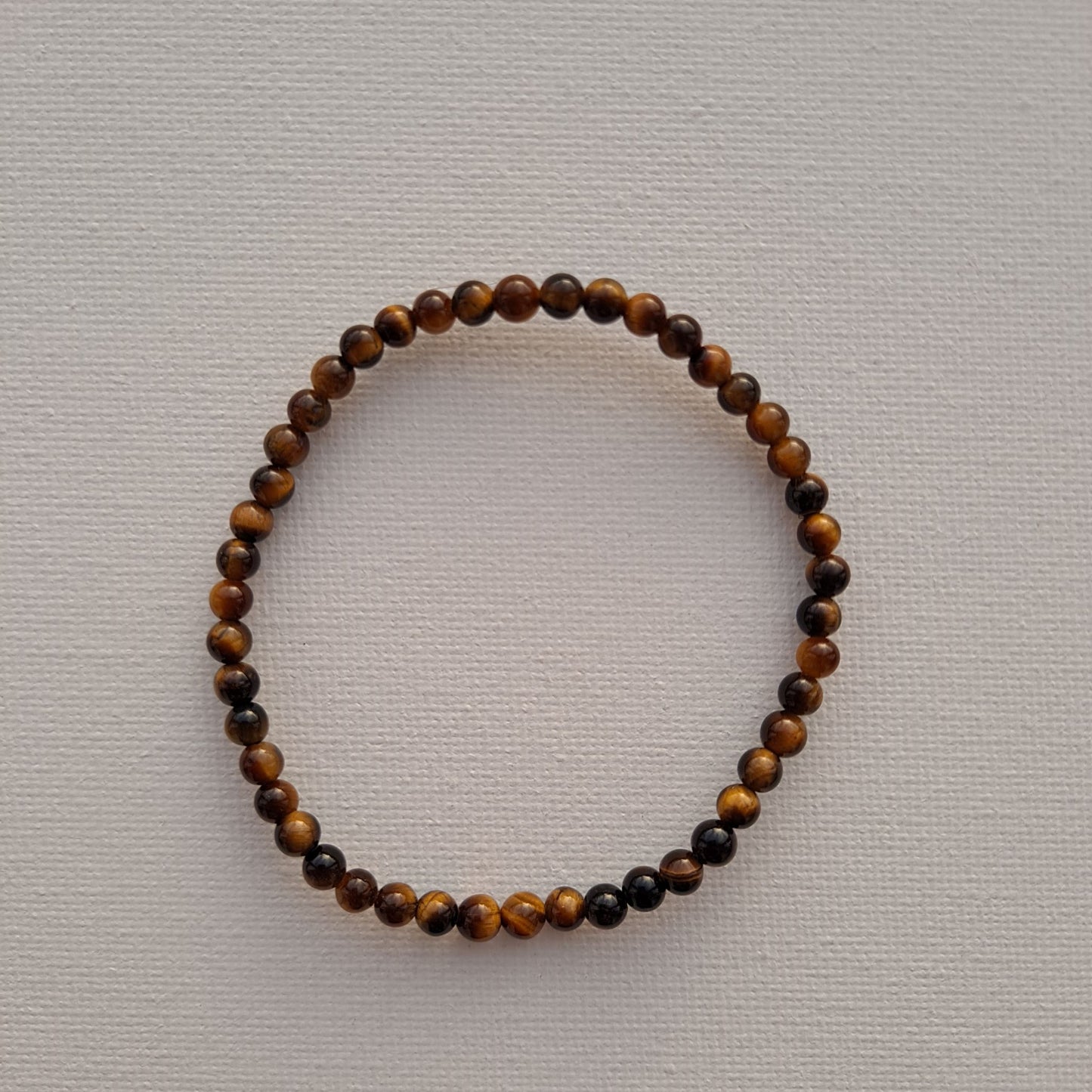 Dumi's Crystals | Tiger's Eye Stretch Bracelet (7 Inch with 4mm Beads) | Close-up of a handcrafted bracelet featuring genuine 4mm Tiger's Eye beads with golden-brown hues and a touch of shimmer. Tiger's Eye is known as the stone of courage and protection and is believed to promote strength, confidence, mental clarity, and prosperity.