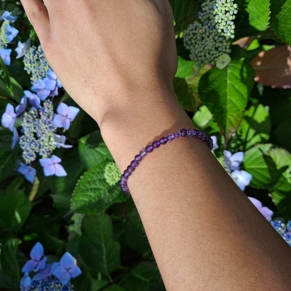 on a hand a beaded amethyst bracelet, green leaves and flowers in the background