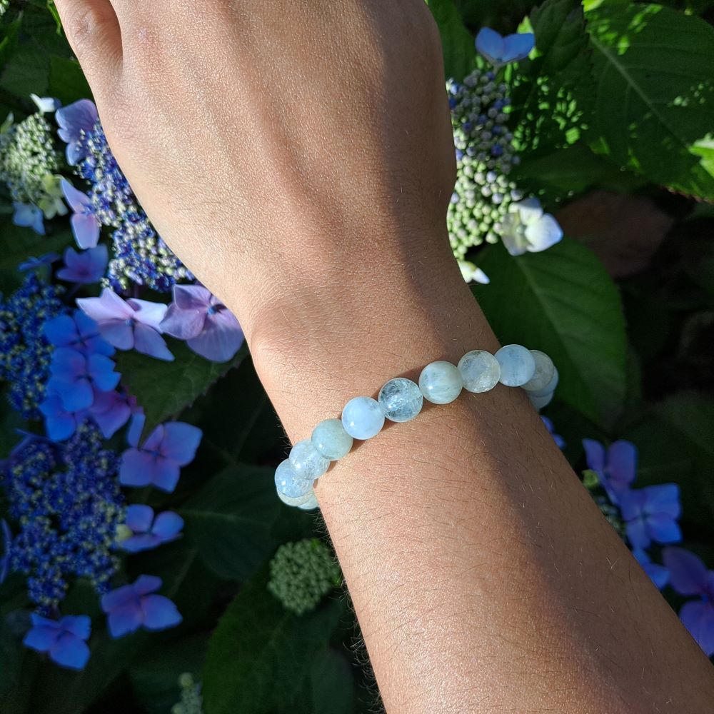 hand showing an aquamarine beaded stretch bracelet, green leaves and purple flowers in the background