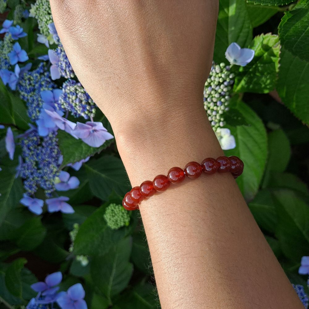 hand wearing a carnelian beaded stretch bracelet, green leaves and purple flowers in the background