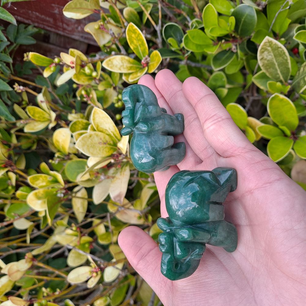 hand showing two green aventurine elephants carvings, green leaves in the background