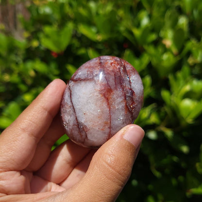 Hand holding a fire quartz palm  stone against a green leafy background