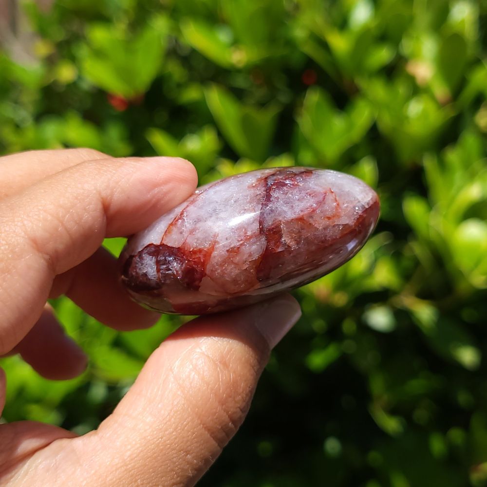 Hand holding a hematoid quartz palm stone with a green blurred background