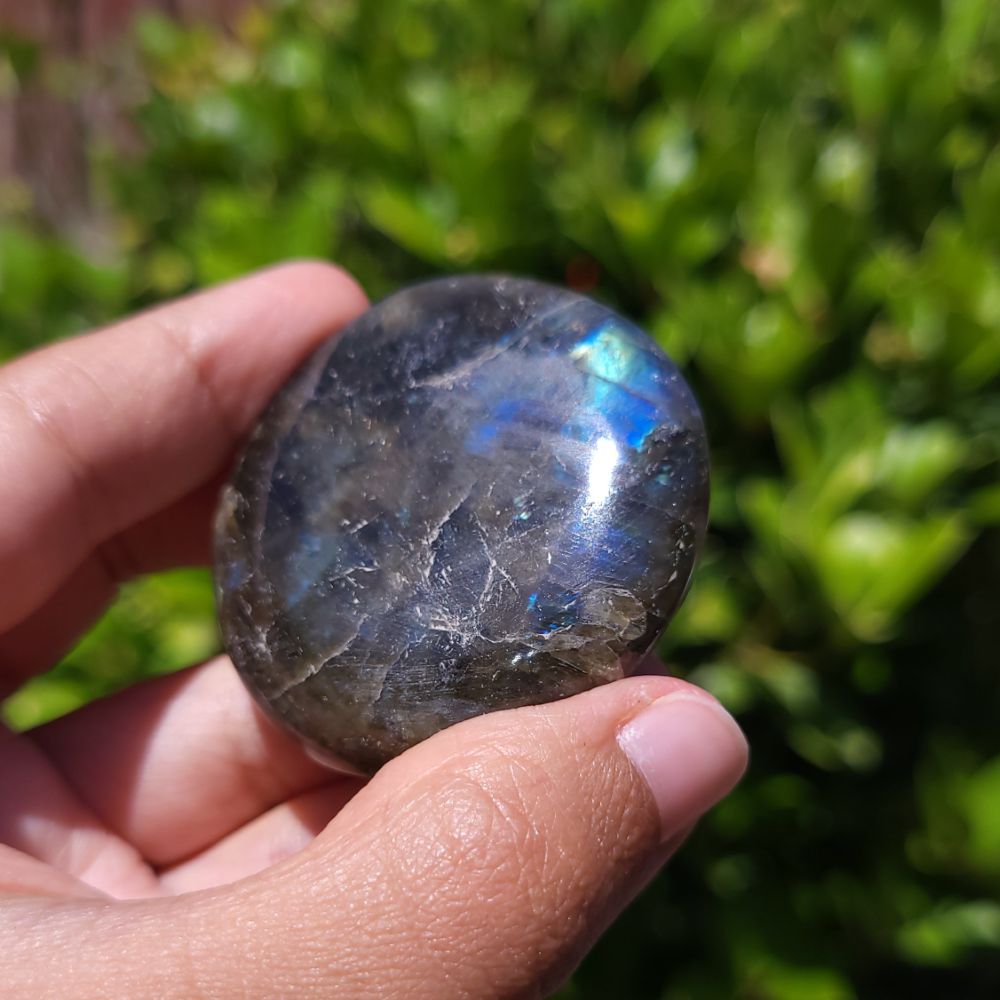 Hand holding a Labradorite stone with a blurred green background