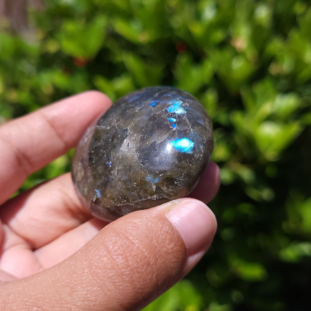 Hand holding a labradorite stone with a blurred green background