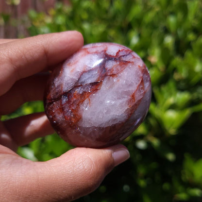 Hand holding a Hematoid Quartz palm stone with a blurred green background