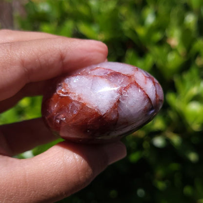 Hand holding a Hematoid Quartz palm stone with a green blurred background