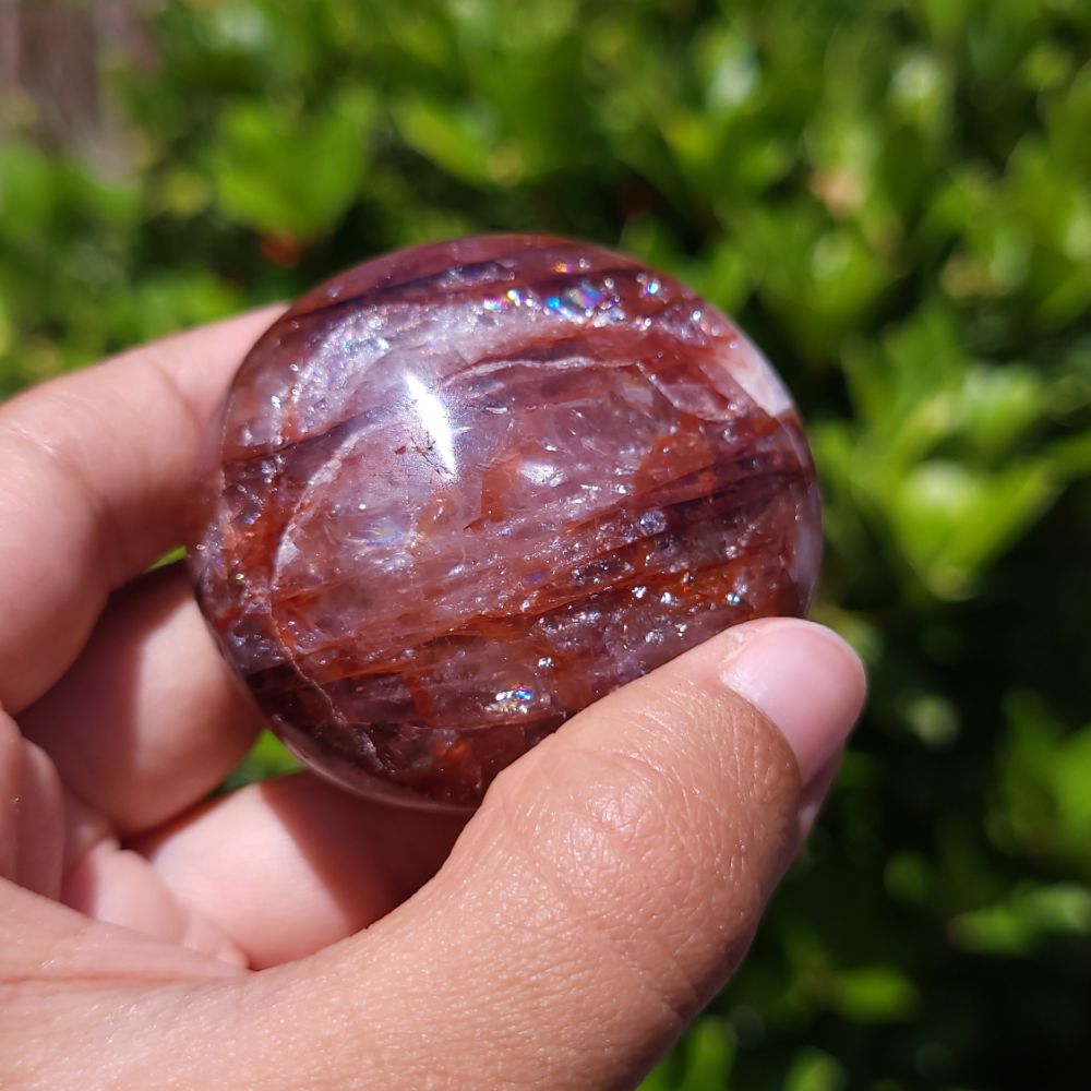 Hand holding a polished Hematoid Quartz palm stone a green outdoor background