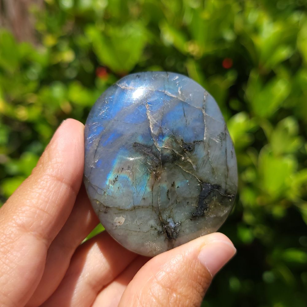 Hand holding a labradorite stone with a blurred green background