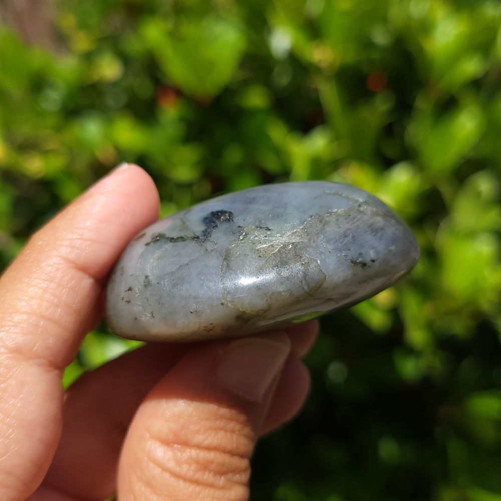 Hand holding a blue stone with a blurred green background