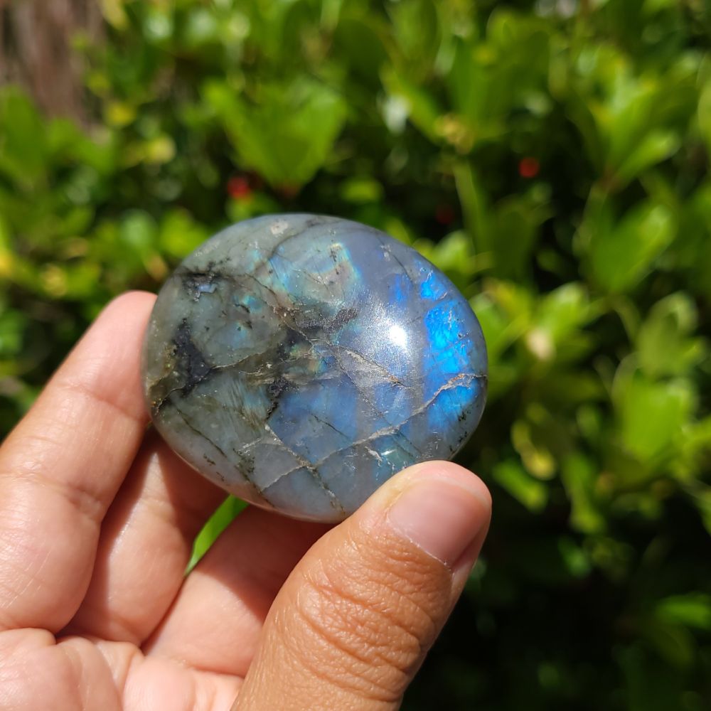 Hand holding a labradorite stone with a blurred green background