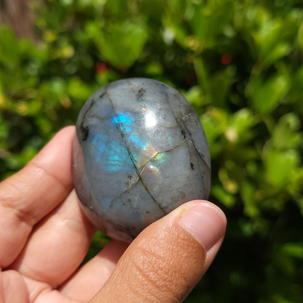 Labradorite stone held in a hand with a blurred green outdoor background