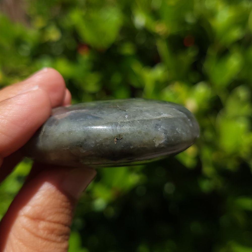 Hand holding a labradorite palm stone with a blurred green background