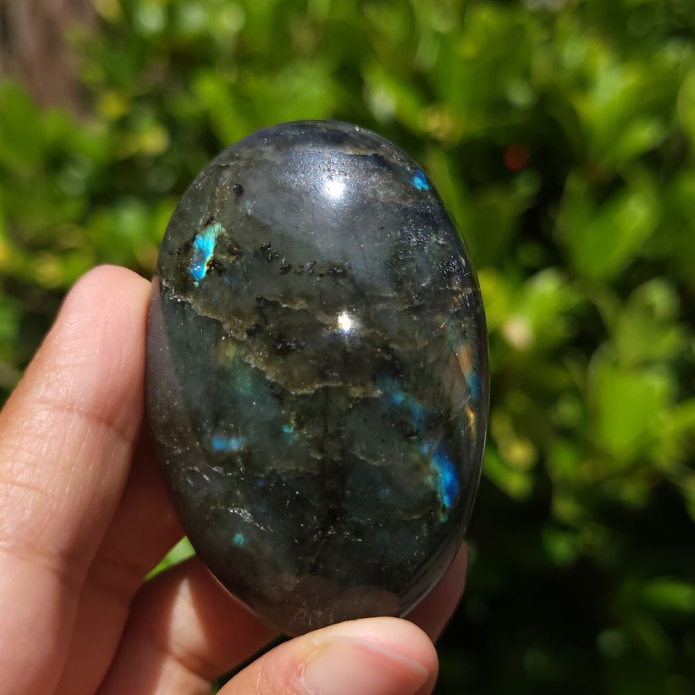 Person holding a labradorite stone with a blurred green background