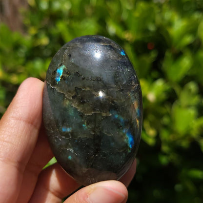 Person holding a labradorite stone with a blurred green background