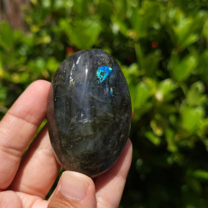 Person holding a labradorite stone with a green and blue pattern against a blurred natural background