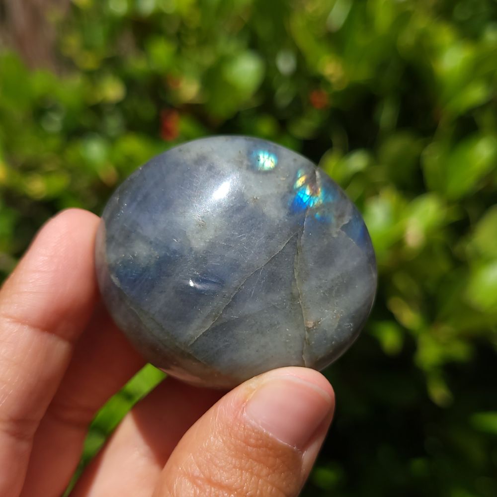 Blue labradorite stone held in a hand with a blurred green background