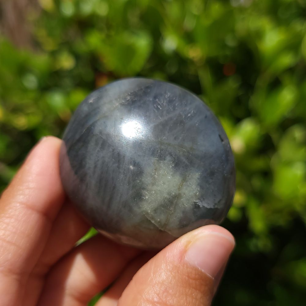 Person holding a labradorite palm stone sphere with a blurred green background