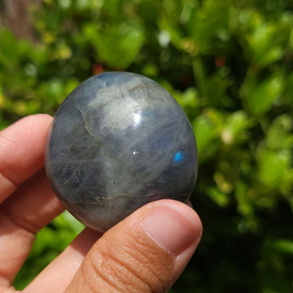 Hand holding a Labradorite stone with a blurred green background