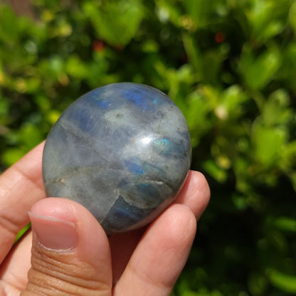 Hand holding a labradorite stone with a blurred green outdoor background