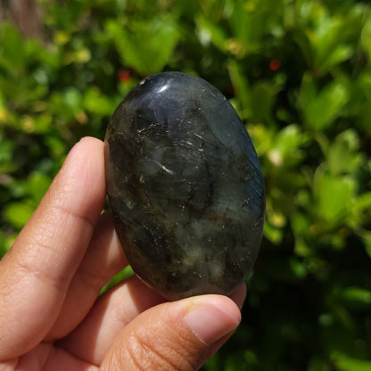 Hand holding a labradorite palm stone with a blurred green background